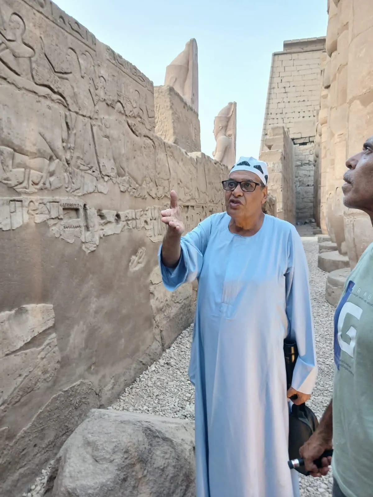 An Egyptian guide explaining ancient wall reliefs to a traveler at a Luxor temple