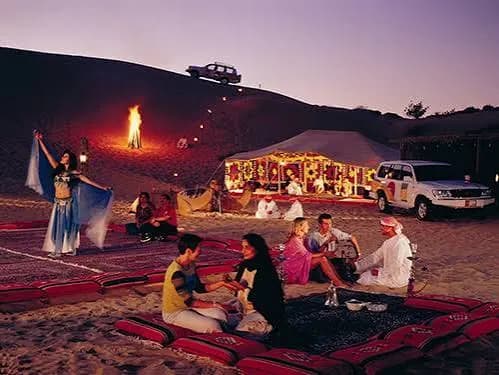 Tourists gathered around a campfire at a Bedouin desert camp at dusk